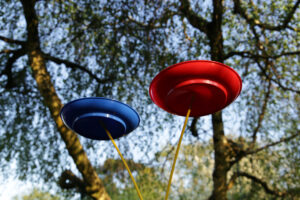 A red and a blue plate balanced on sticks beneath trees