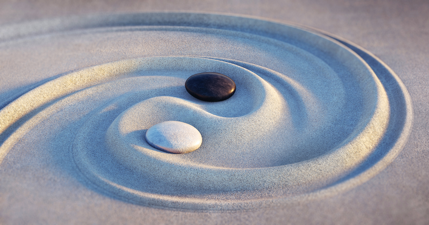 Spiral drawn in sand with two smooth rocks in the middle