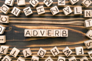 Adverb - word from wooden blocks with letters, describes or gives more information concept, random letters around, top view on wooden background