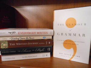 Books in a stack: Everybody Writes, Writing Down the Bownes, The Writer's Journey, The Sense of Style, Vex, Hex, Smash, Smooch. One book standing upright: The Glamour of Grammar