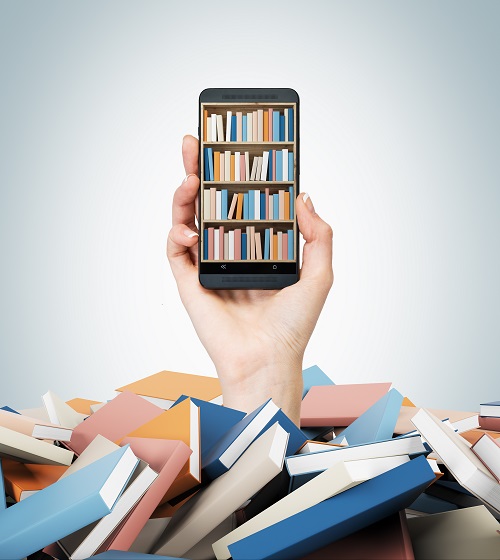 Pile of colorful books with a white hand reaching out. The hand holds a cell phone with an image of a full bookshelf on it.