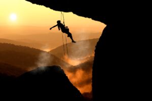 Woman in silhouette dangling from ropes while she mountain climbs